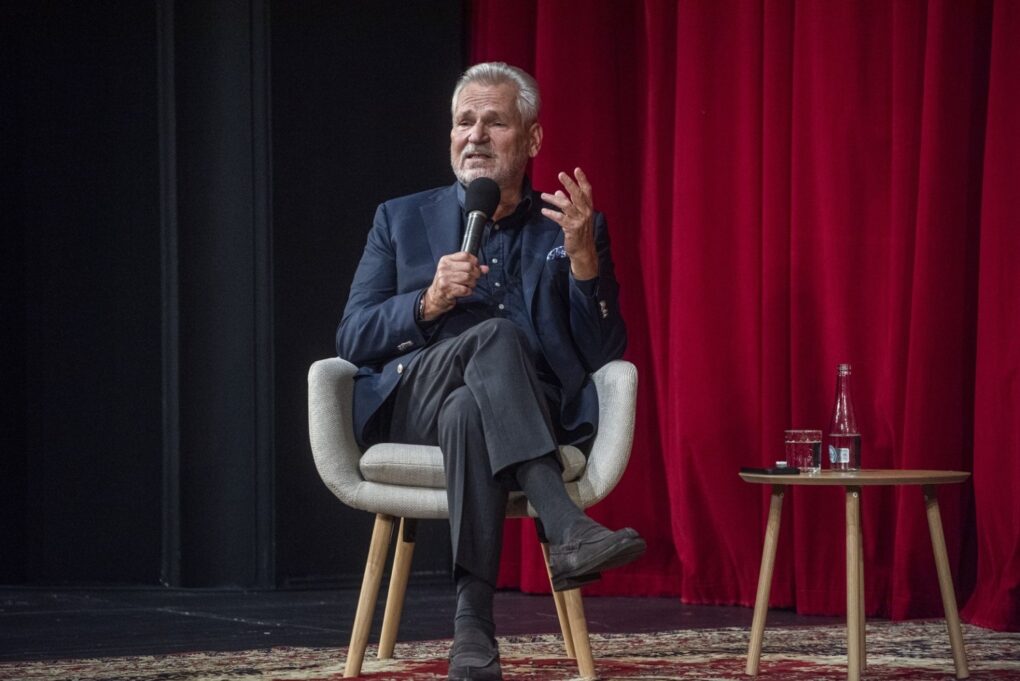 Alenksander Kwaśniewski siedzi na scenie i przemawia do mikrofonu podczas spotkania w teatrze (kliknięcie powiększy zdjęcie).