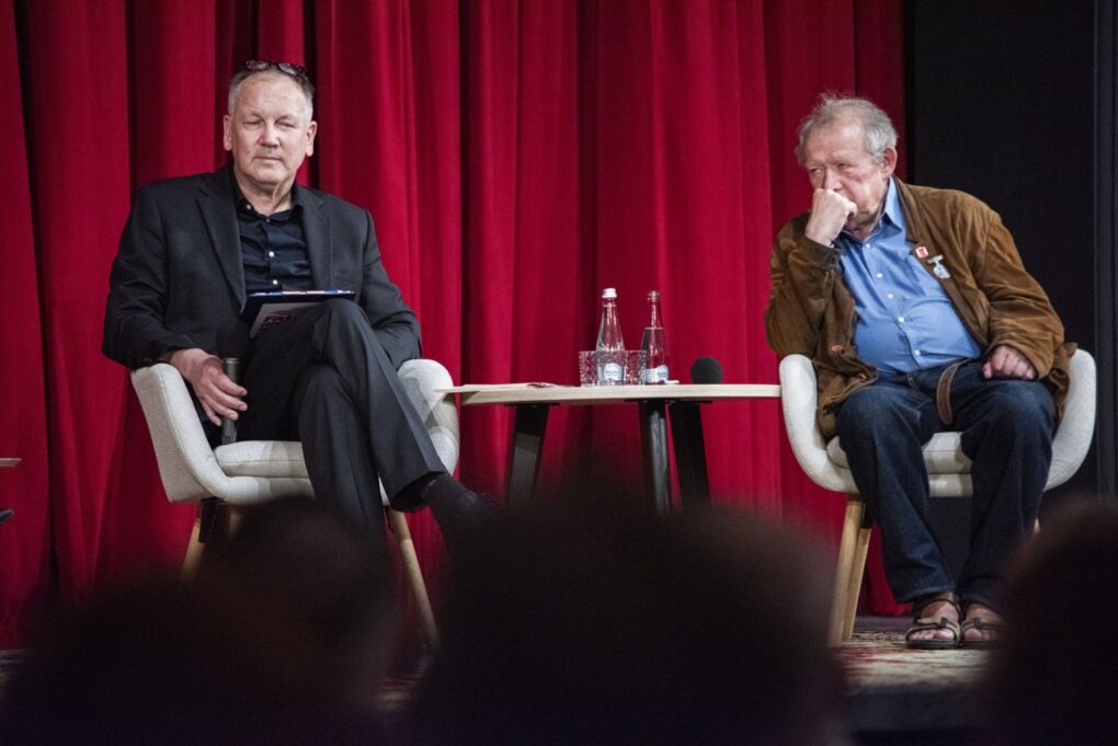 Dwóch uczestników debaty siedzi na scenie i bierze udział w dyskusji (kliknięcie powiększy zdjęcie).