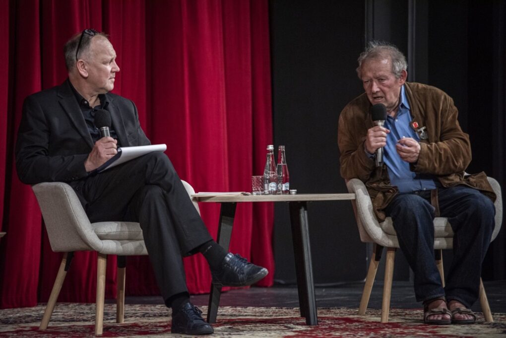 Prowadzący i uczestnik debaty rozmawiają na scenie podczas spotkania (kliknięcie powiększy zdjęcie).