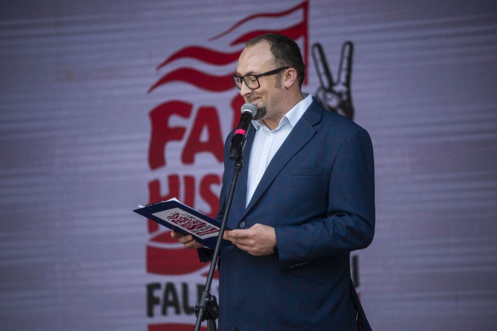 Mężczyzna w garniturze przemawia do mikrofonu na scenie podczas wydarzenia „Fale Historii” (kliknięcie powiększy zdjęcie).