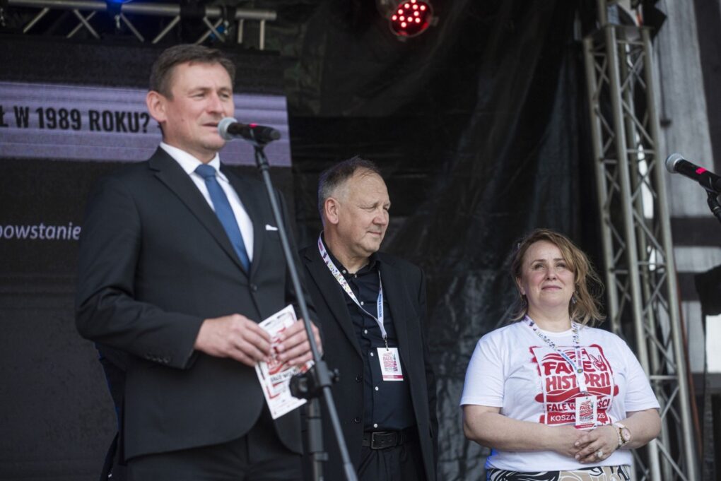Prezydent Koszalina przemawia na scenie do publiczności, obok stoją organizatorzy wydarzenia (kliknięcie powiększy zdjęcie).