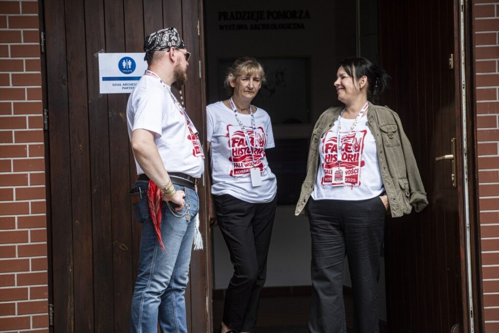 Trzy osoby stoją przy wejściu do budynku i rozmawiają ze sobą (kliknięcie powiększy zdjęcie).