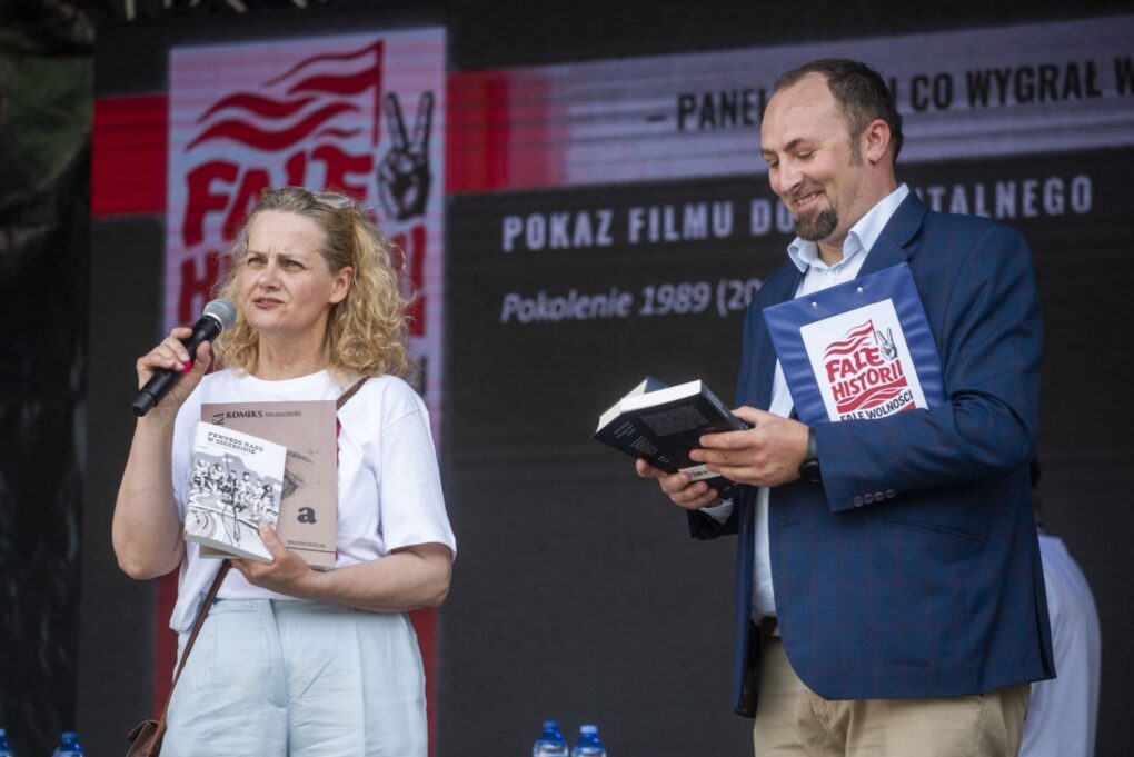Kobieta i mężczyzna na scenie prezentują książkę i prowadzą rozmowę podczas wydarzenia „Fale Historii” (kliknięcie powiększy zdjęcie).