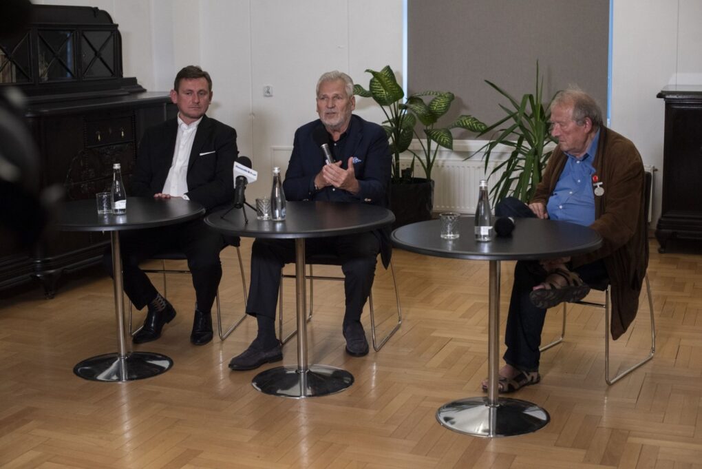 Trzech mężczyzn siedzi przy stolikach i prowadzi dyskusję po spotkaniu (kliknięcie powiększy zdjęcie).