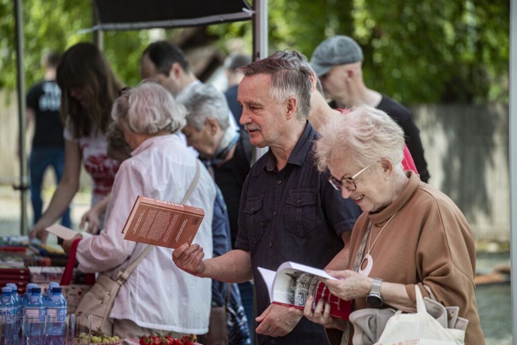 Uczestnicy przeglądają książki i materiały na stoisku podczas wydarzenia plenerowego (kliknięcie powiększy zdjęcie).