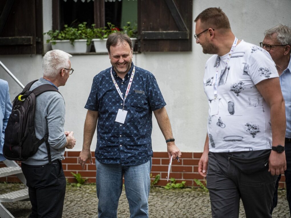 Trzy osoby uśmiechają się i rozmawiają na dziedzińcu przy budynku muzeum (kliknięcie powiększy zdjęcie).