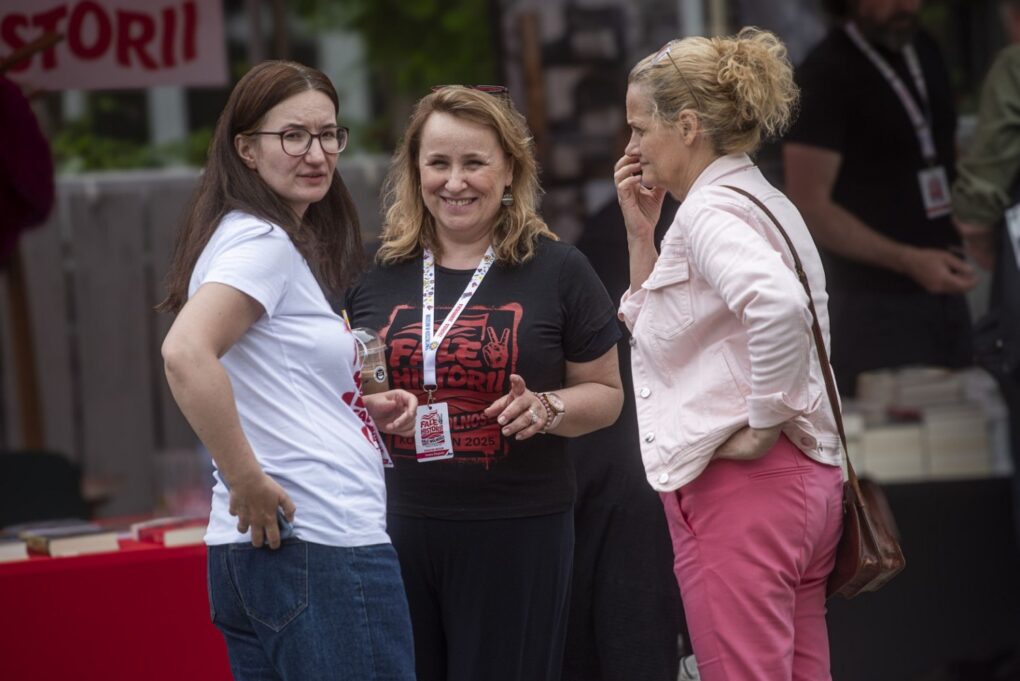 Trzy uczestniczki wydarzenia rozmawiają i stoją przy stoisku podczas „Fal Historii” (kliknięcie powiększy zdjęcie).