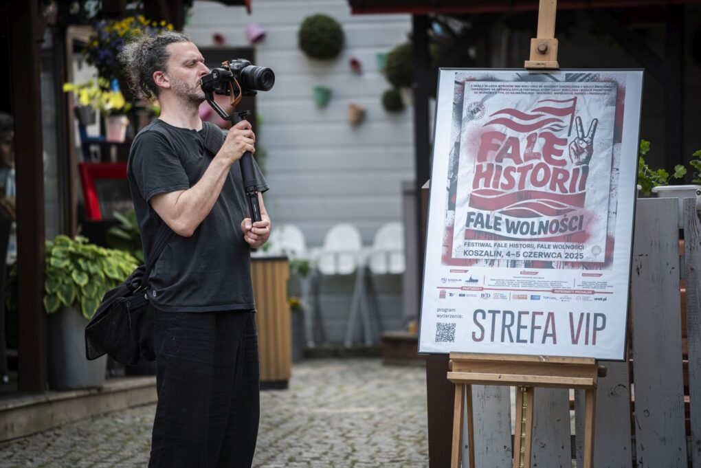 Fotograf wykonuje zdjęcia obok tablicy informacyjnej ze znakiem „Strefa VIP” (kliknięcie powiększy zdjęcie).