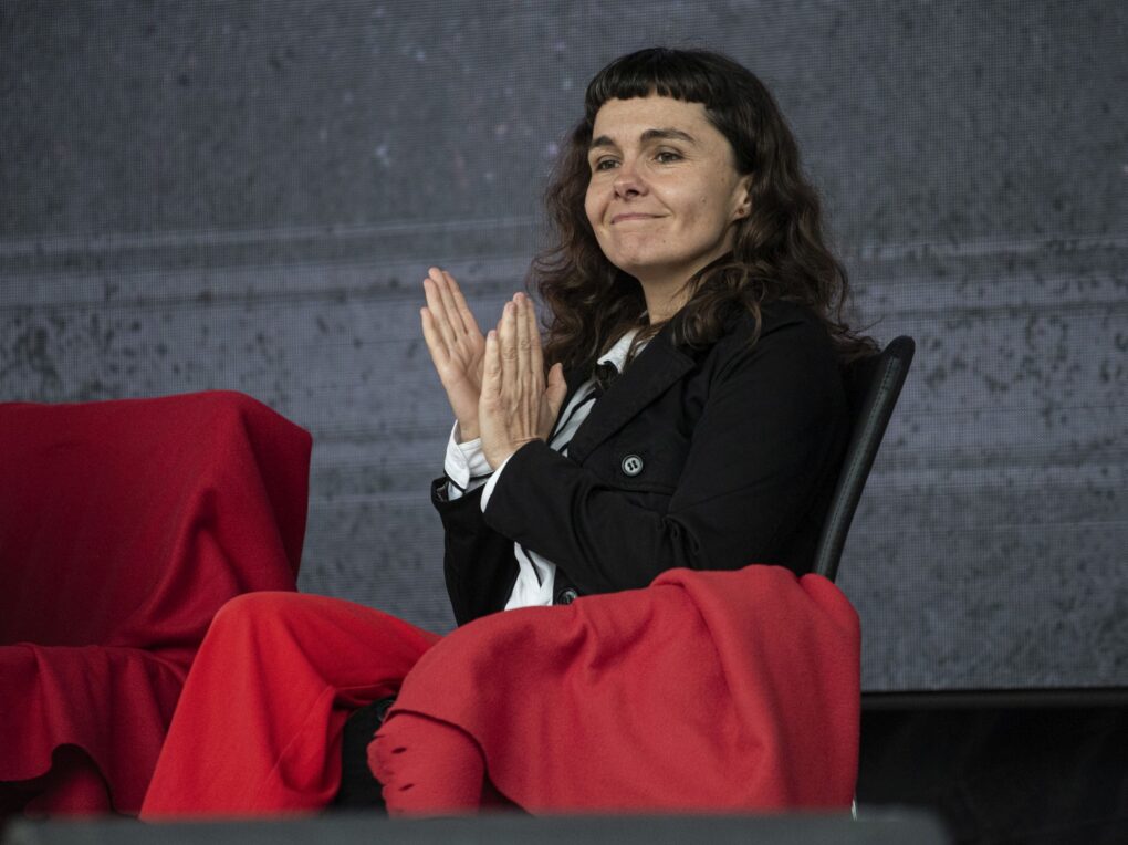 Kobieta siedzi na scenie i bije brawo podczas wydarzenia „Fale Historii” (kliknięcie powiększy zdjęcie).